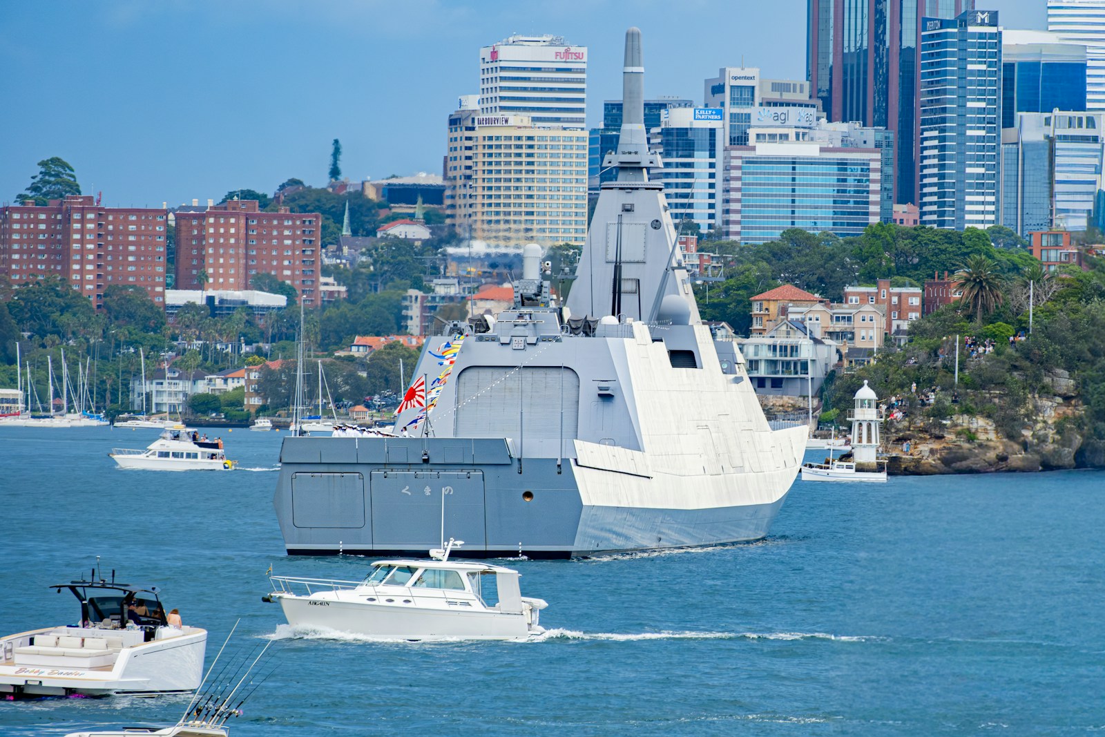 Modern warship sailing in a harbor with city skyline.