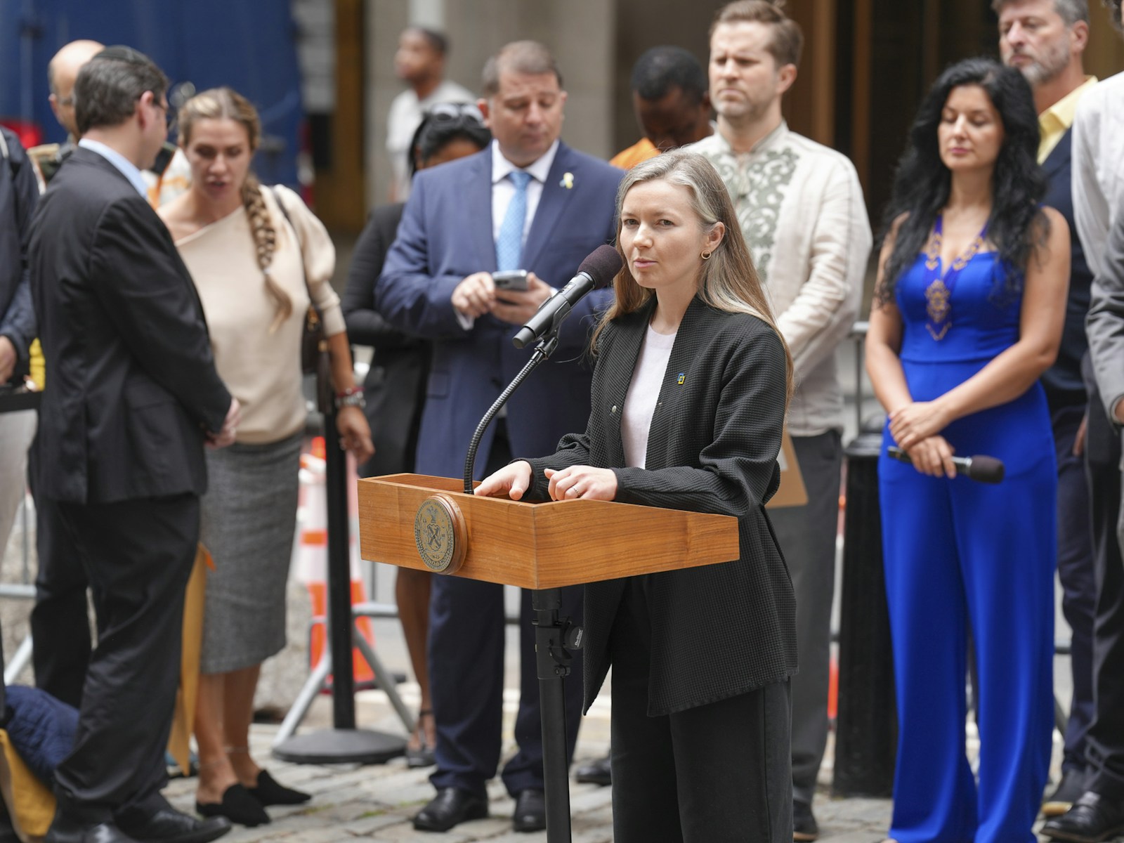 Woman speaks at podium with crowd behind her